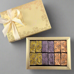 A gold box of Gianduja chocolates with a variety of flavors, including original, with Speculoos biscuit, with almond, and with nougat. The box is adorned with a decorative ribbon and placed on a wooden surface with flowers scattered around.
